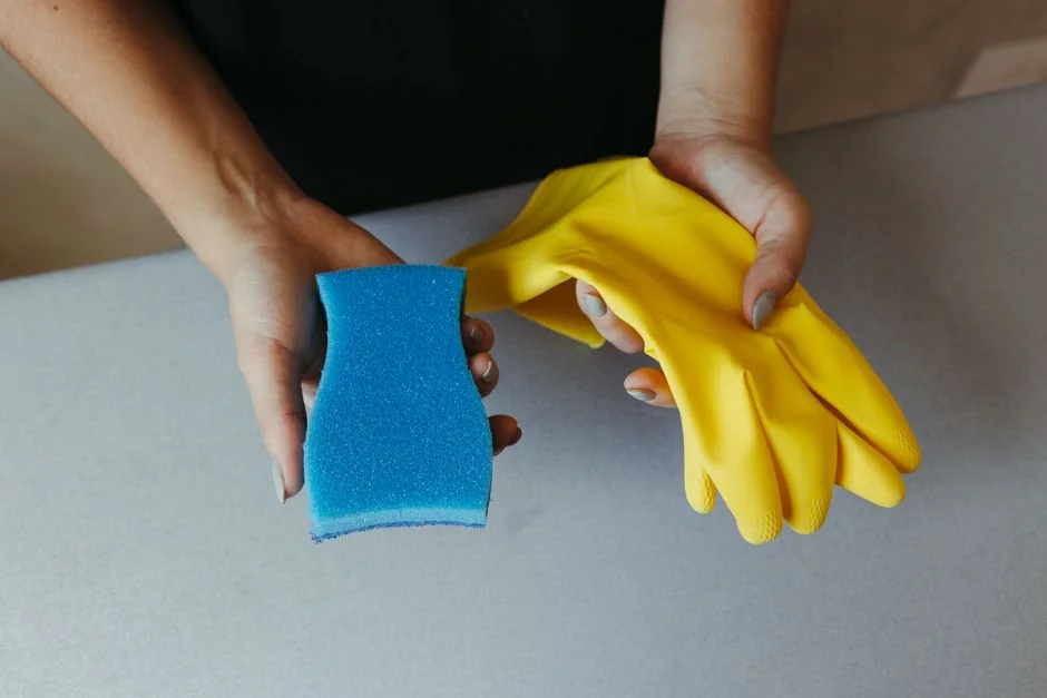 Close-up of hand cleaning window with squeegee outdoors using yellow gloves.
